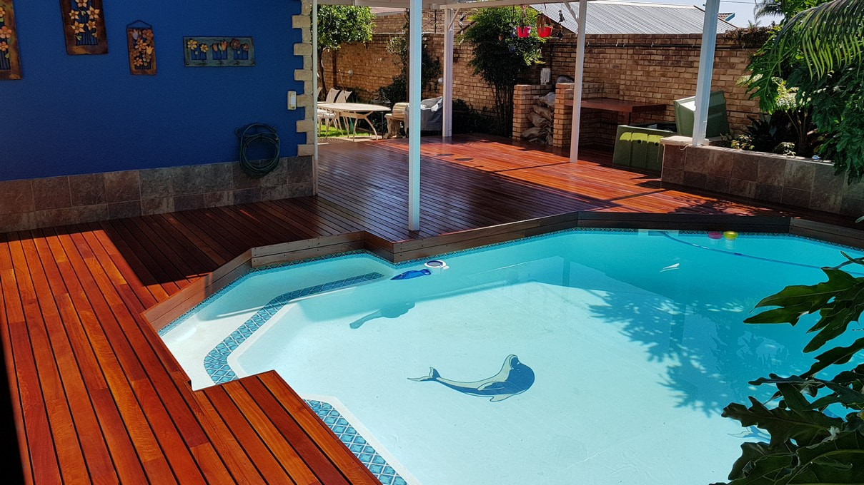 A picturesque outdoor area features a red ironbark pool decking surrounded by lush trees.