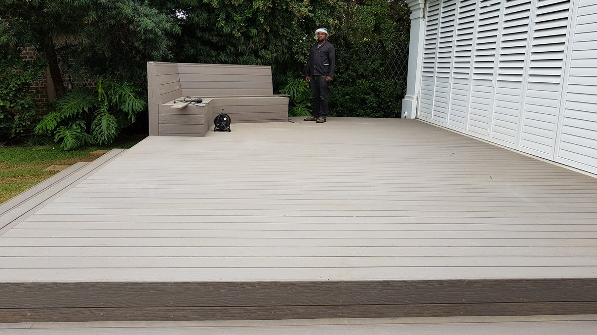 A proud Timbermann employee stands atop a newly crafted MoistureShield composite deck, displaying excellent craftsmanship.